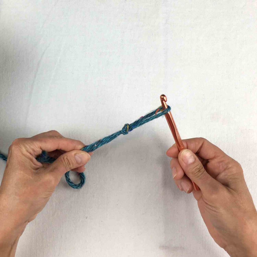 image of hands holding a crochet hook and a green loop