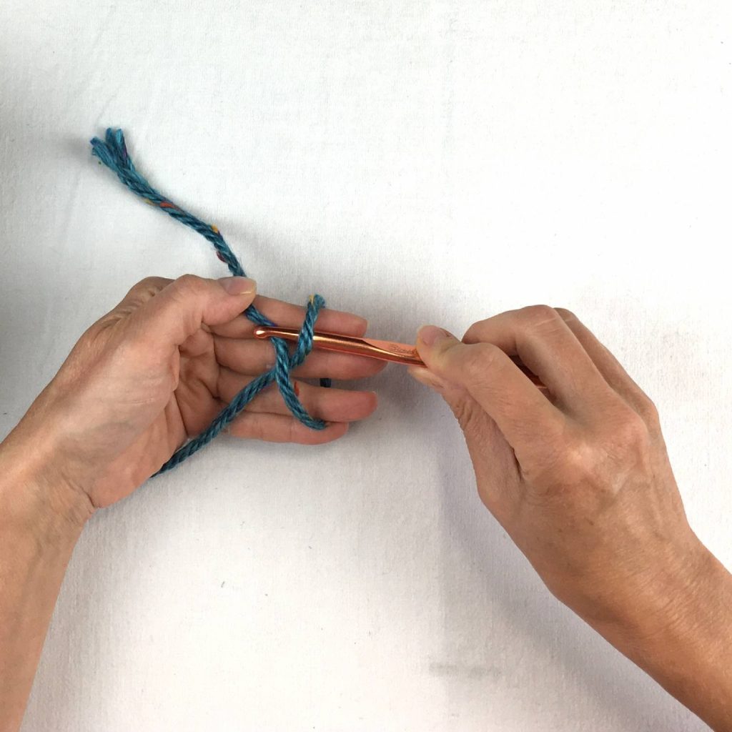 image of green yarn looped over a hand and a crochet hook grabbing one end
