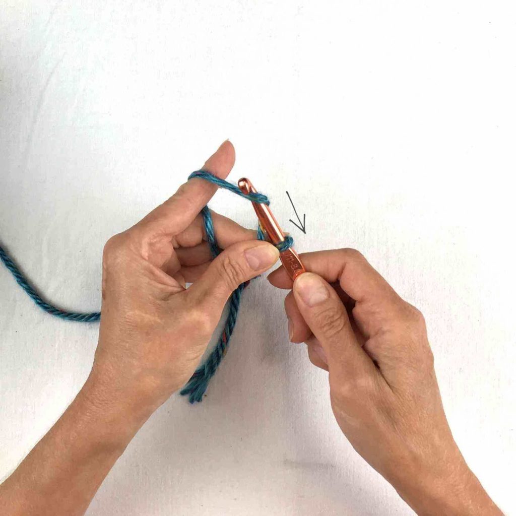 image of hands holding a crochet hook and grabbing green yarn to pull through