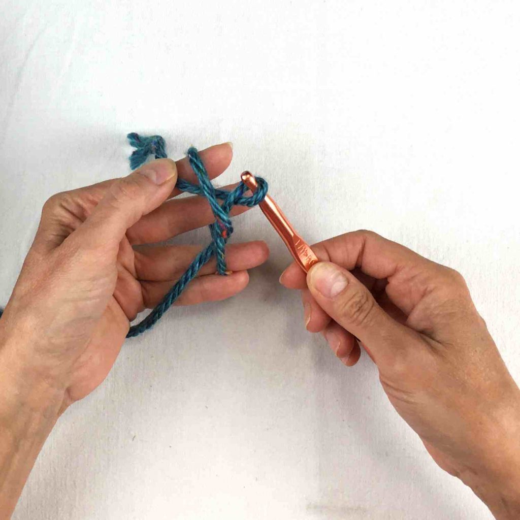 image of two hands holding a crochet hook and a loop of green yarn 