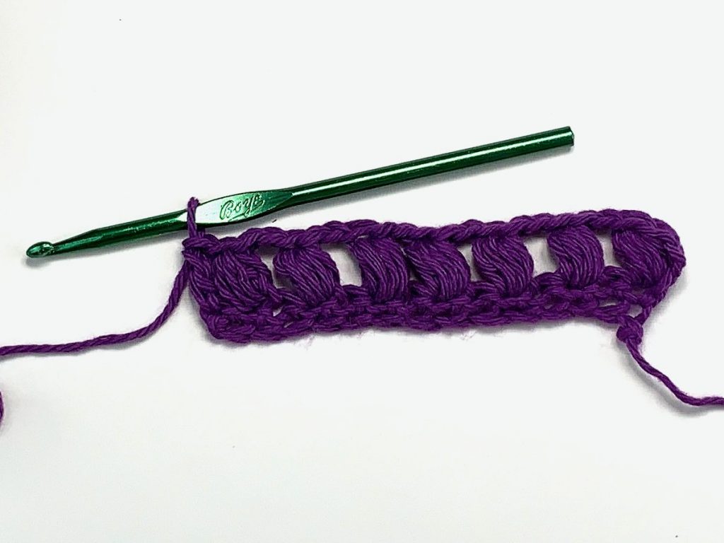 A row of crocheted puff stitches in purple yarn