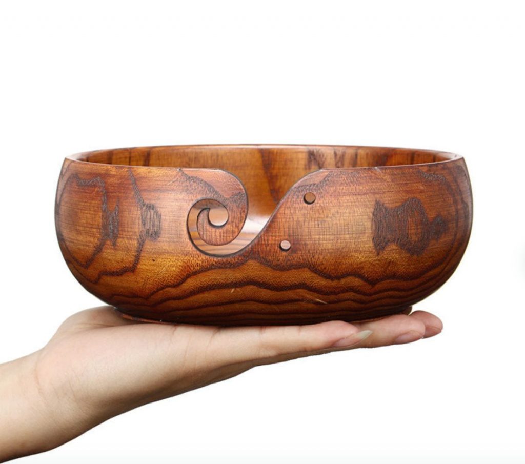 A hand holding a wooden yarn bowl