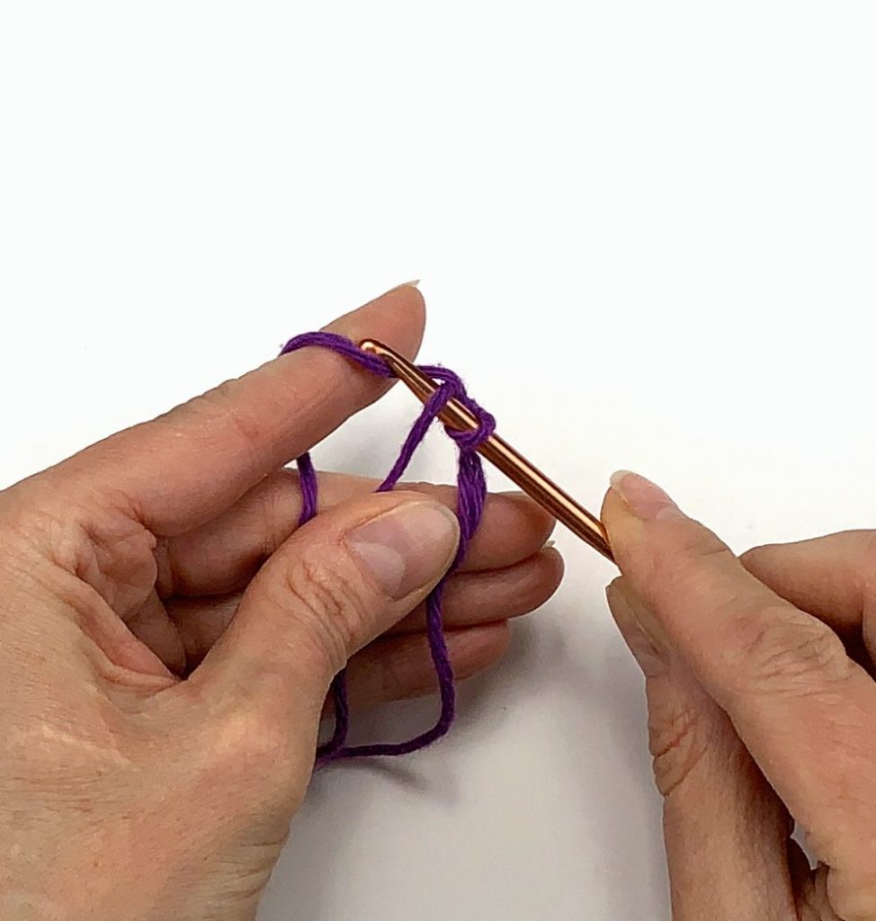 image of two hands crocheting with purple yarn