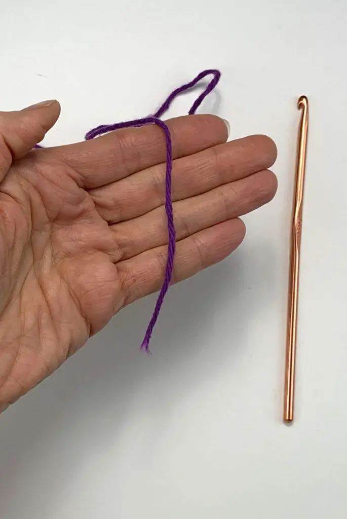 image of a hand with a purple strand of yarn