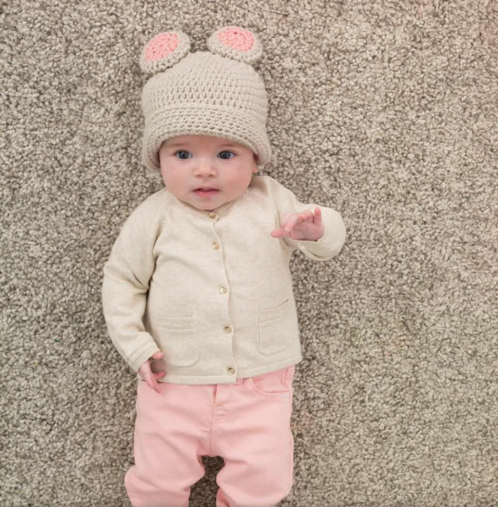 image of a baby girl in pink pants, tan sweater and crochet hat