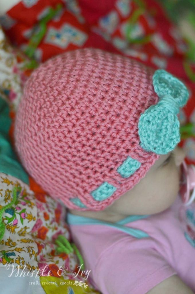 image of a baby wearing a pink crochet hat with blue ribbon