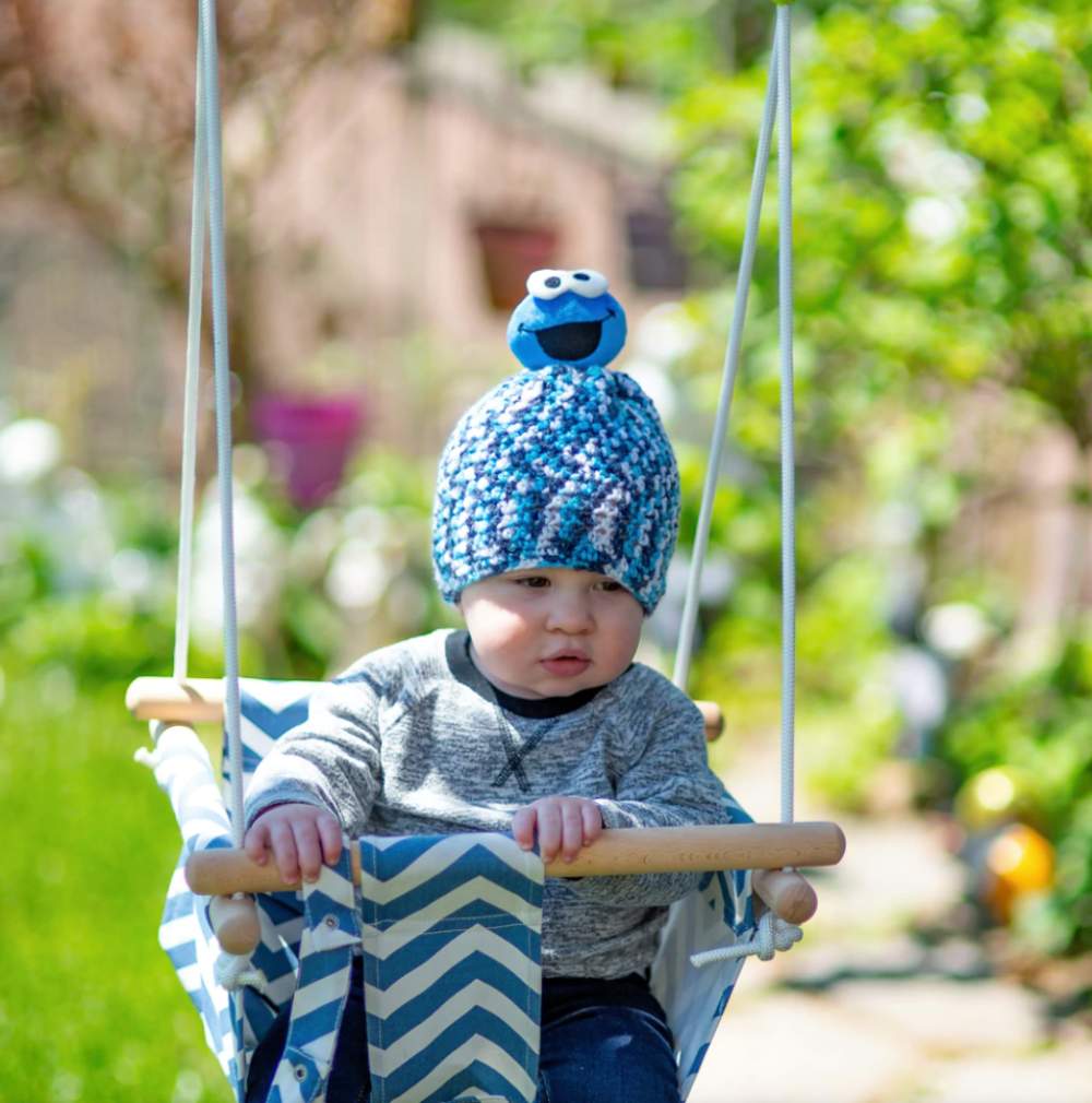 image of a baby boy in a swing with a blue crocheted hat