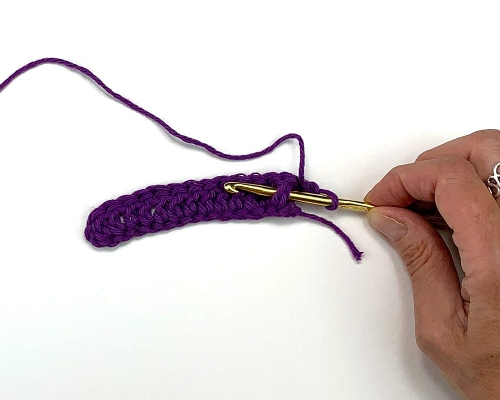 purple crochet work with a crochet hook showing the post