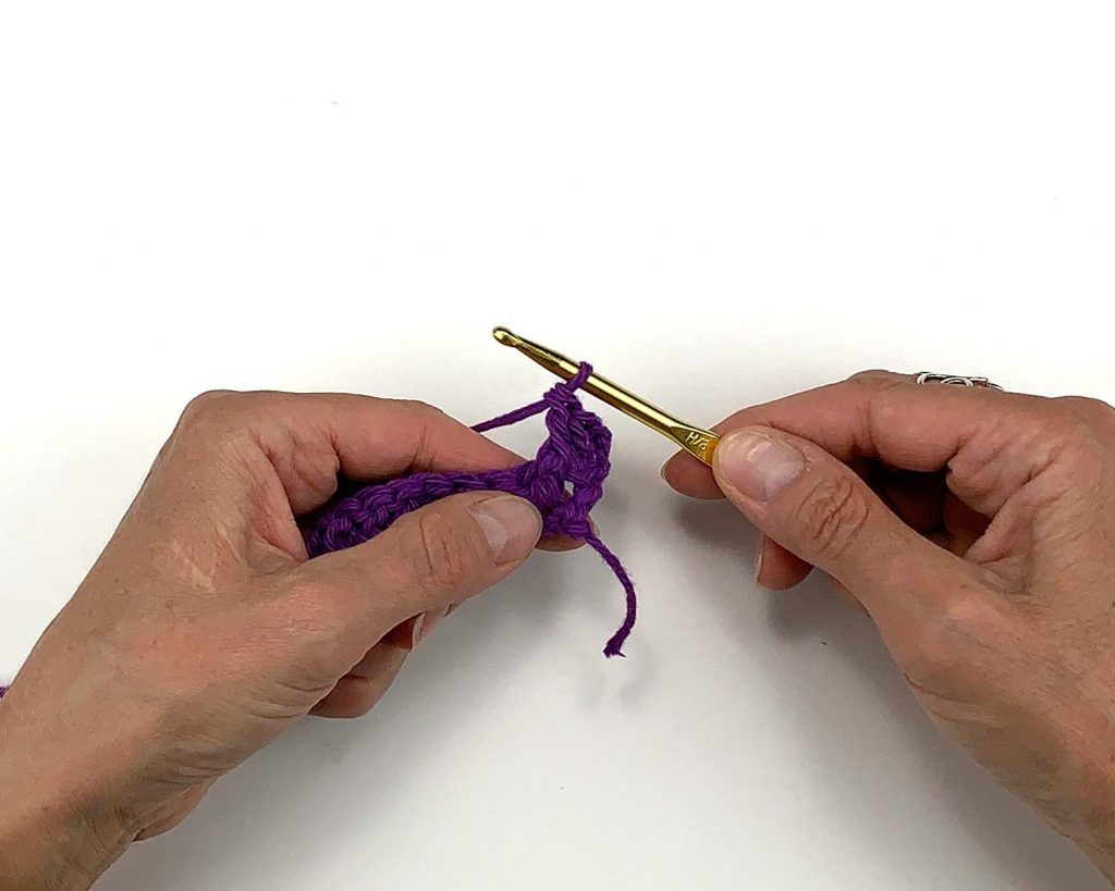 image of hands holding purple yarn crochet work